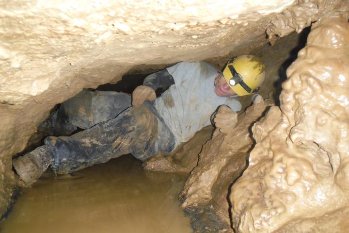 Man crawling through tight spot in cave