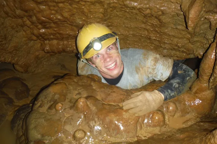 Man covered in mud crawling through cave opening